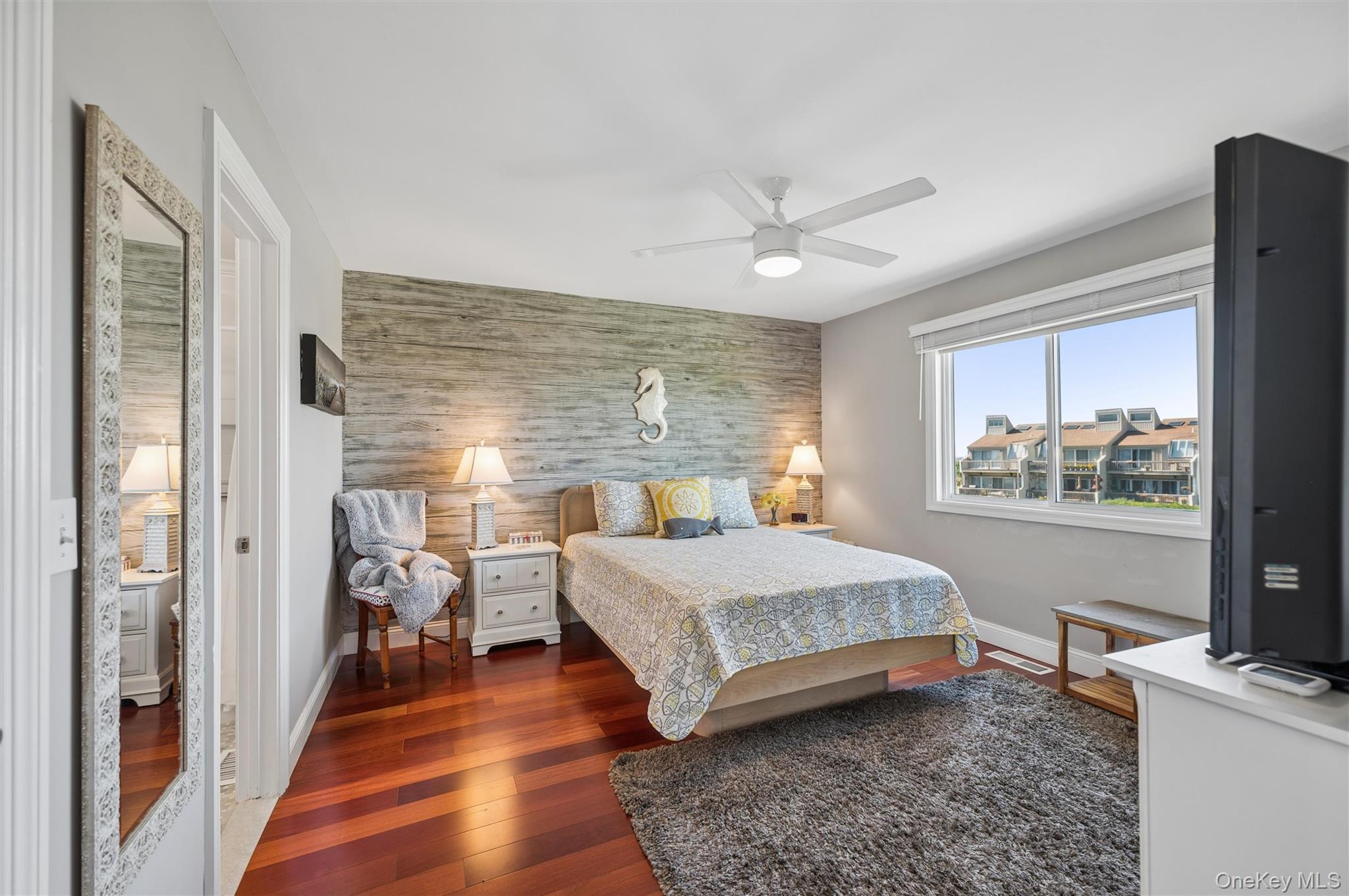 Bedroom with a weathered wood accent wall, hardwood floors, and a window overlooking neighboring homes.