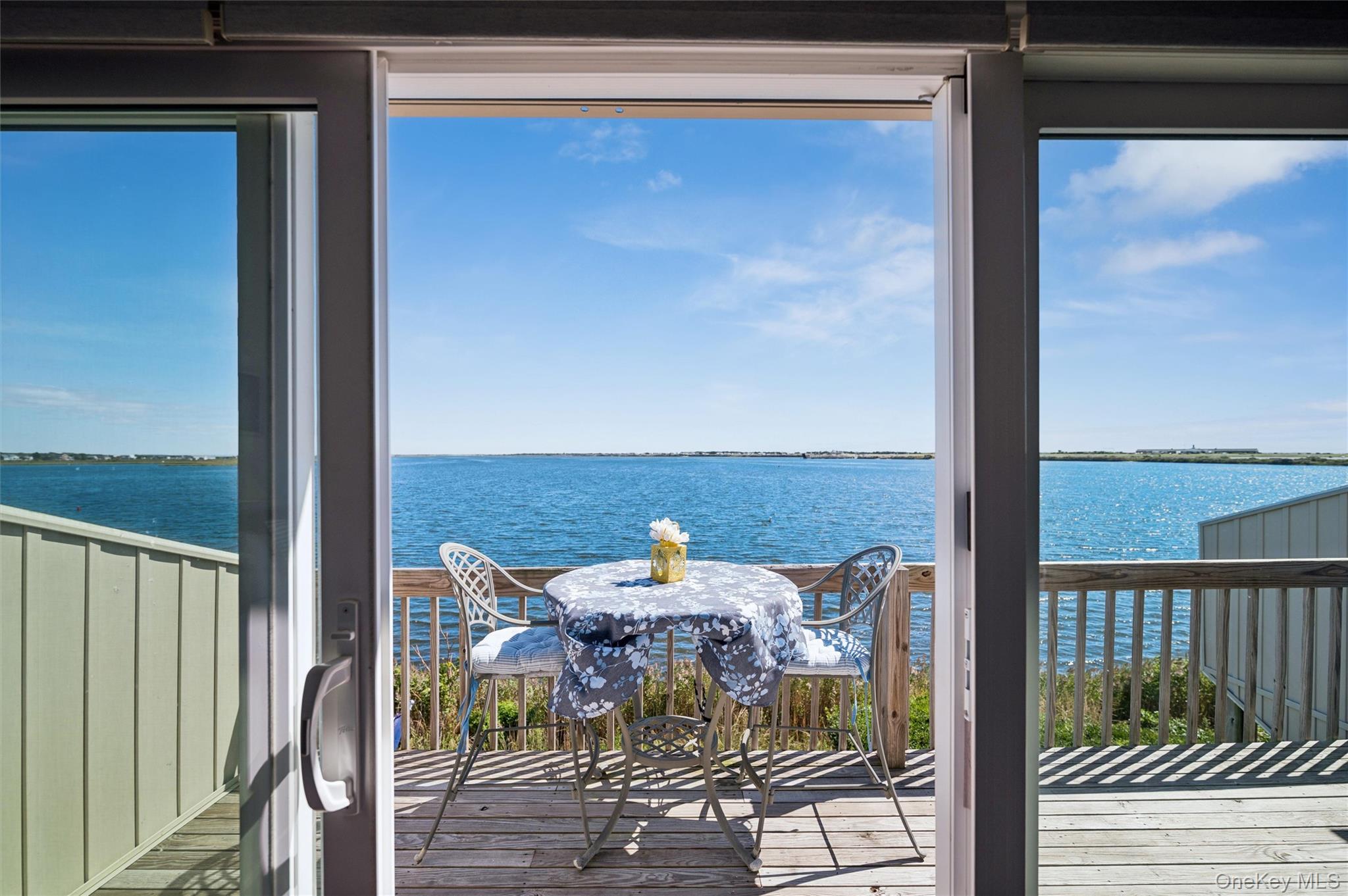 Waterfront deck dining area with two chairs and a table overlooking blue water.