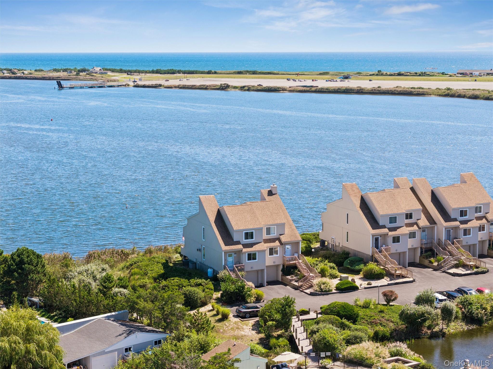 Waterfront homes beside a broad inlet, with the ocean and distant shoreline beyond.