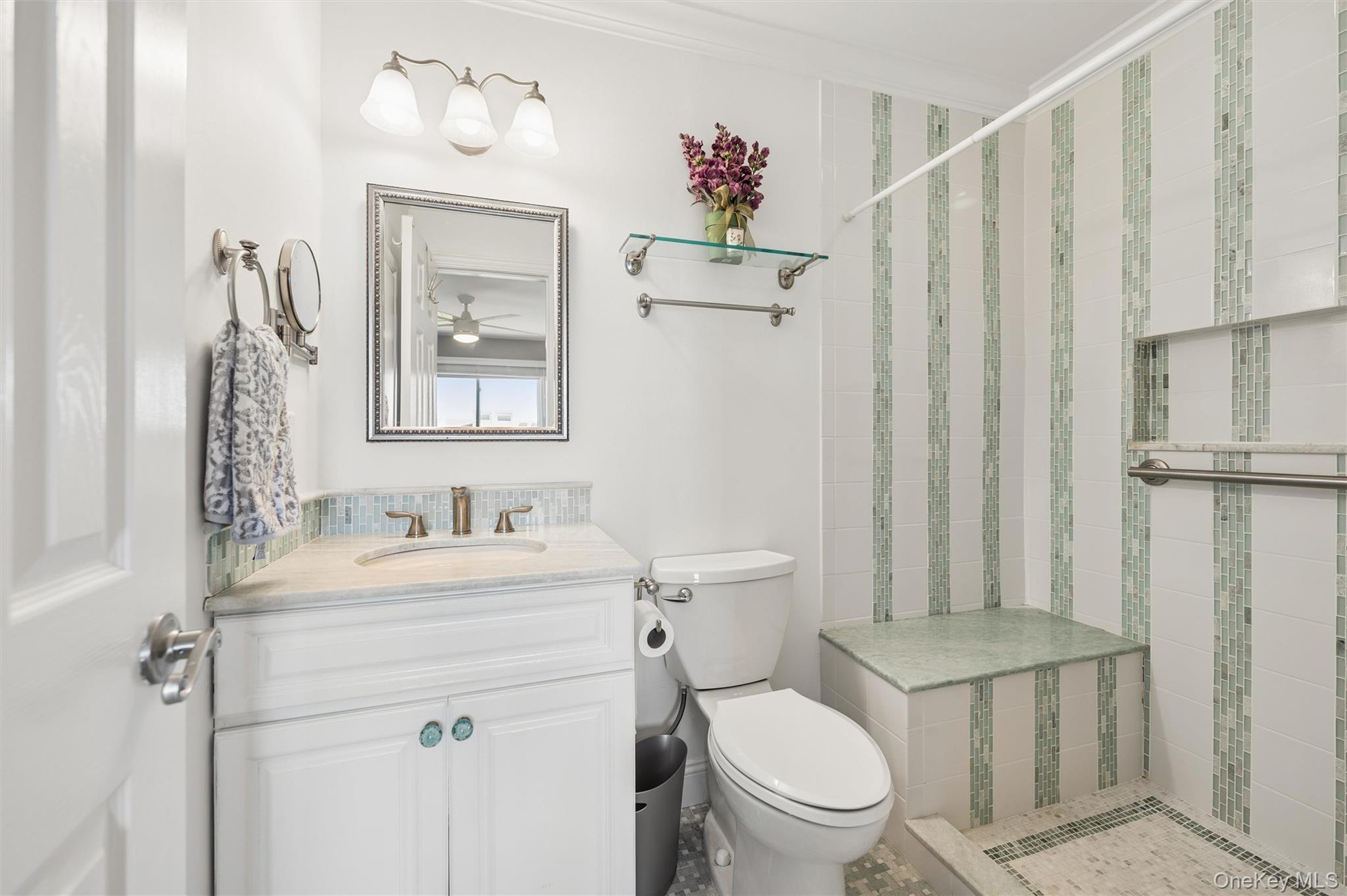 Bathroom with a white vanity and a tiled walk-in shower with green mosaic accents and a built-in bench.