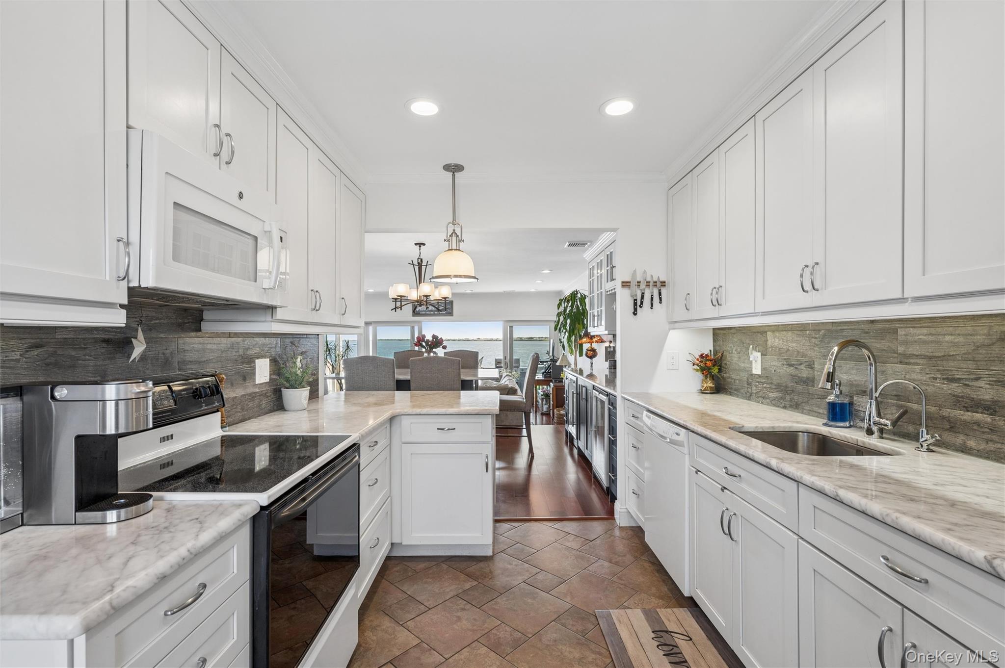 Bright white kitchen with marble counters and water visible beyond the dining area.