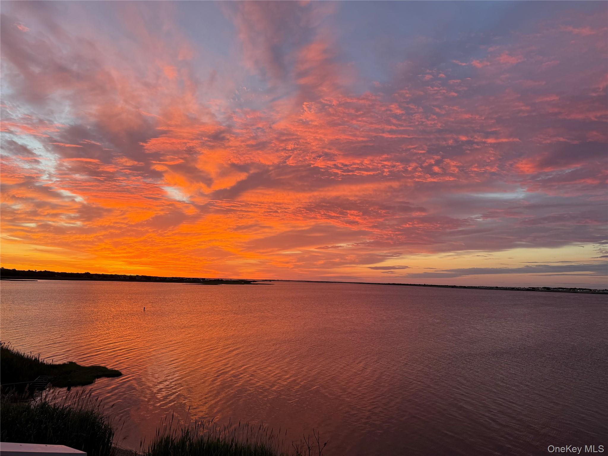 Bay water and shoreline beneath vivid orange and pink sunset clouds.