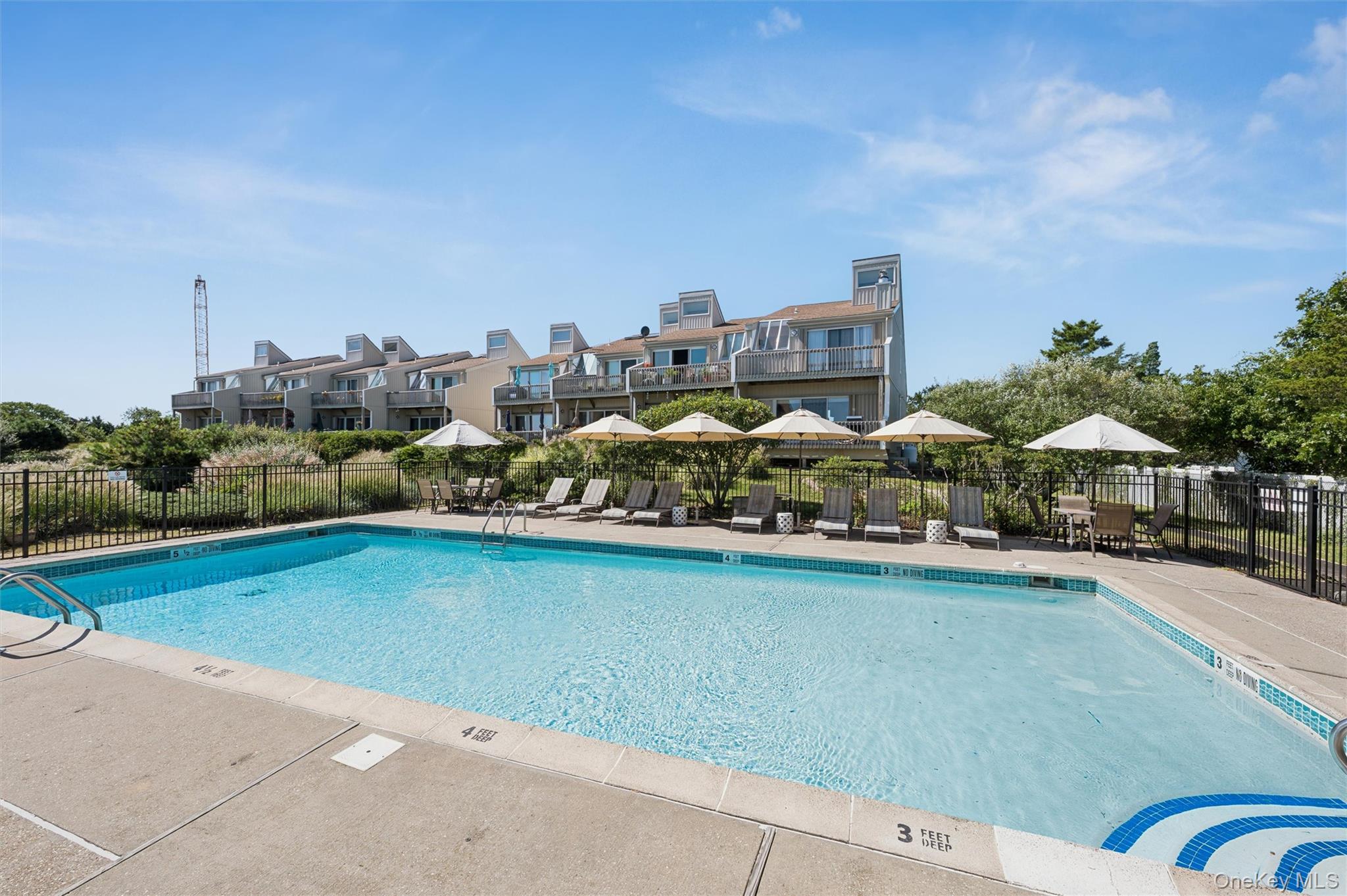 Outdoor pool with loungers and umbrellas in front of attached homes.