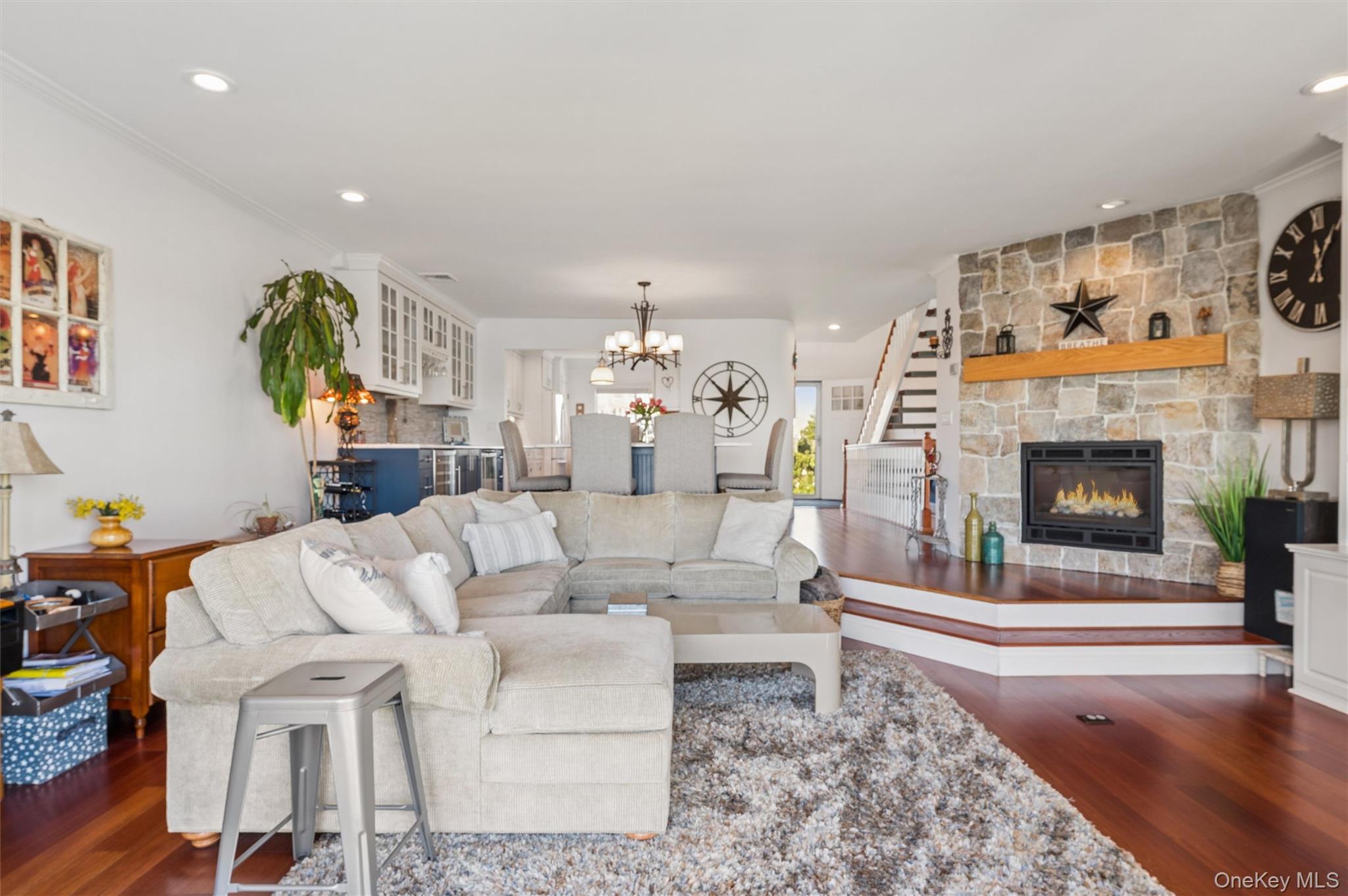 Living room with a cream sectional, stone fireplace, and adjoining kitchen and dining area.
