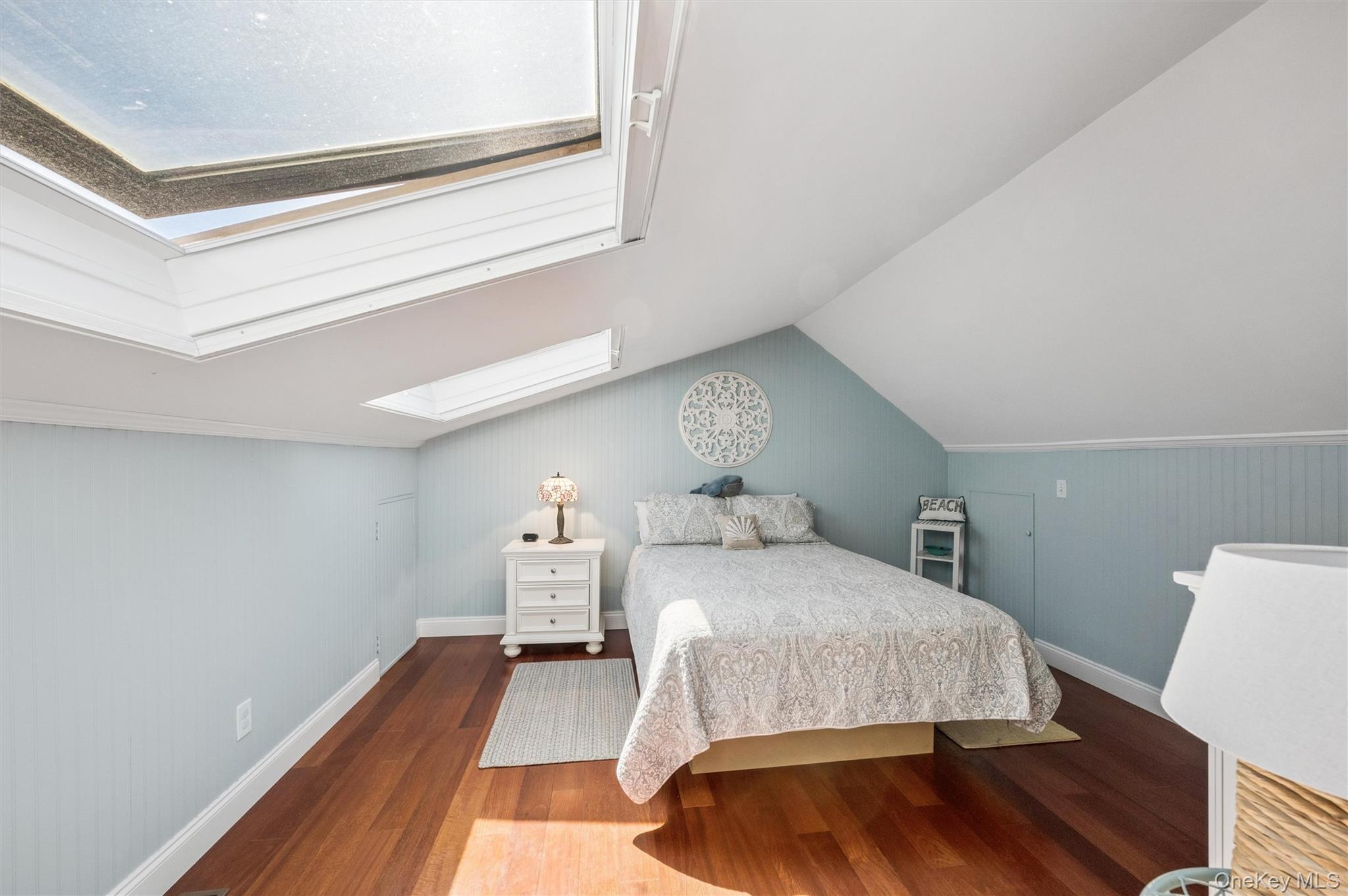 Bedroom with pale blue walls, a skylight, and a patterned bedspread.