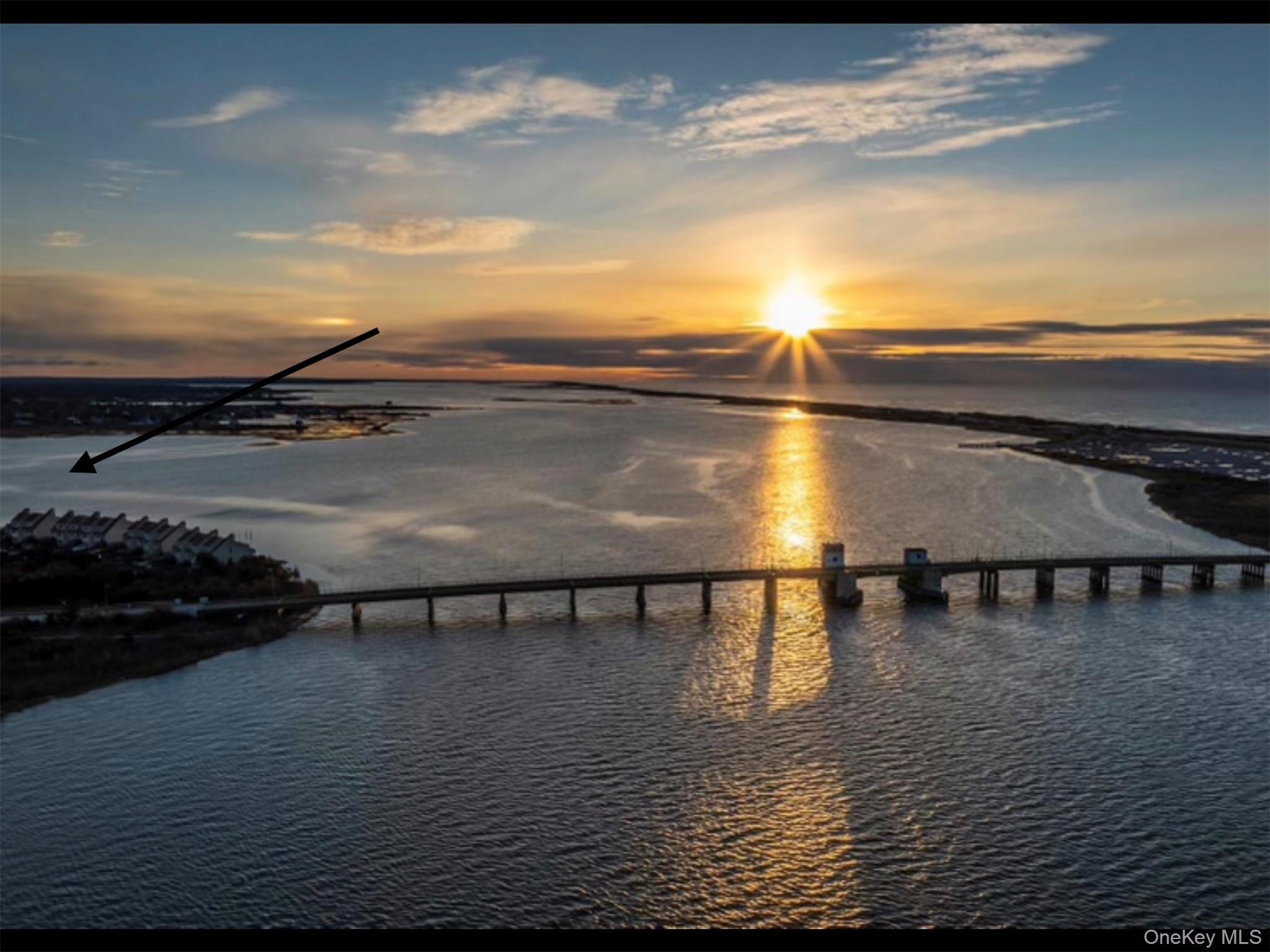 Aerial waterway at sunset, with a bridge in the foreground and an arrow pointing toward shoreline homes.