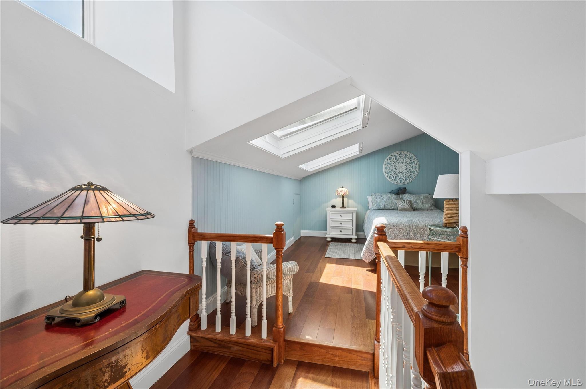 Attic bedroom with skylights, wood floors, and a bed against a pale blue wall.