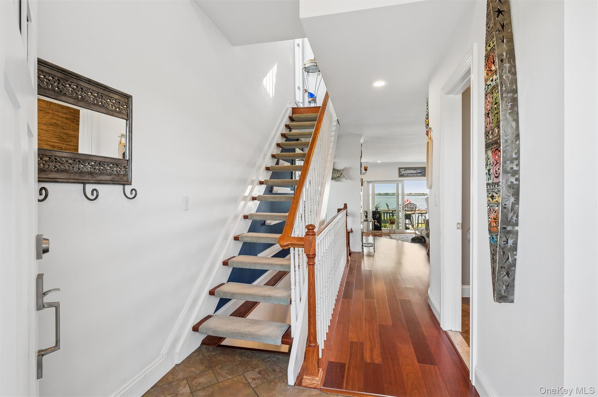 Bright entry hall with an open staircase and water visible through glass doors.