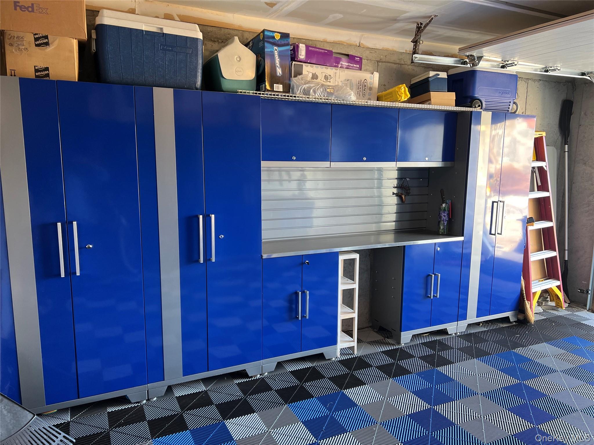 Garage with blue storage cabinets, a stainless-steel workbench, and a patterned floor.