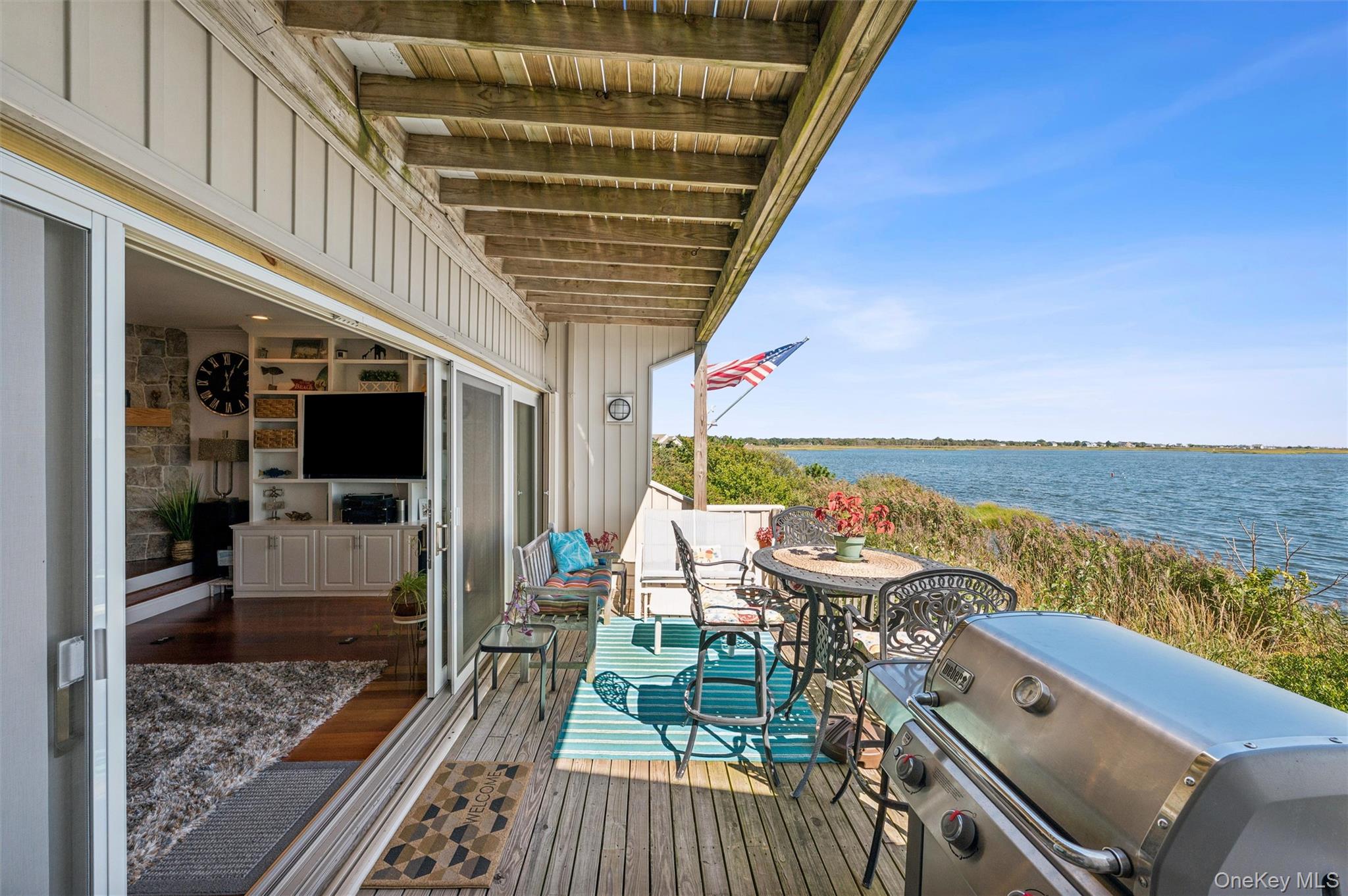 Covered waterfront deck with outdoor dining furniture and a grill overlooking the water.