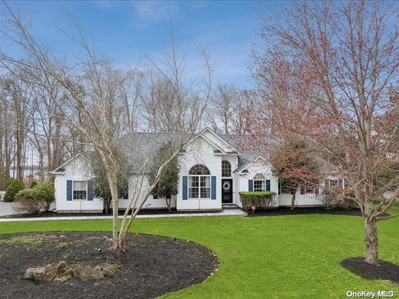 White house with arched windows and blue shutters behind a broad lawn and leafless trees.