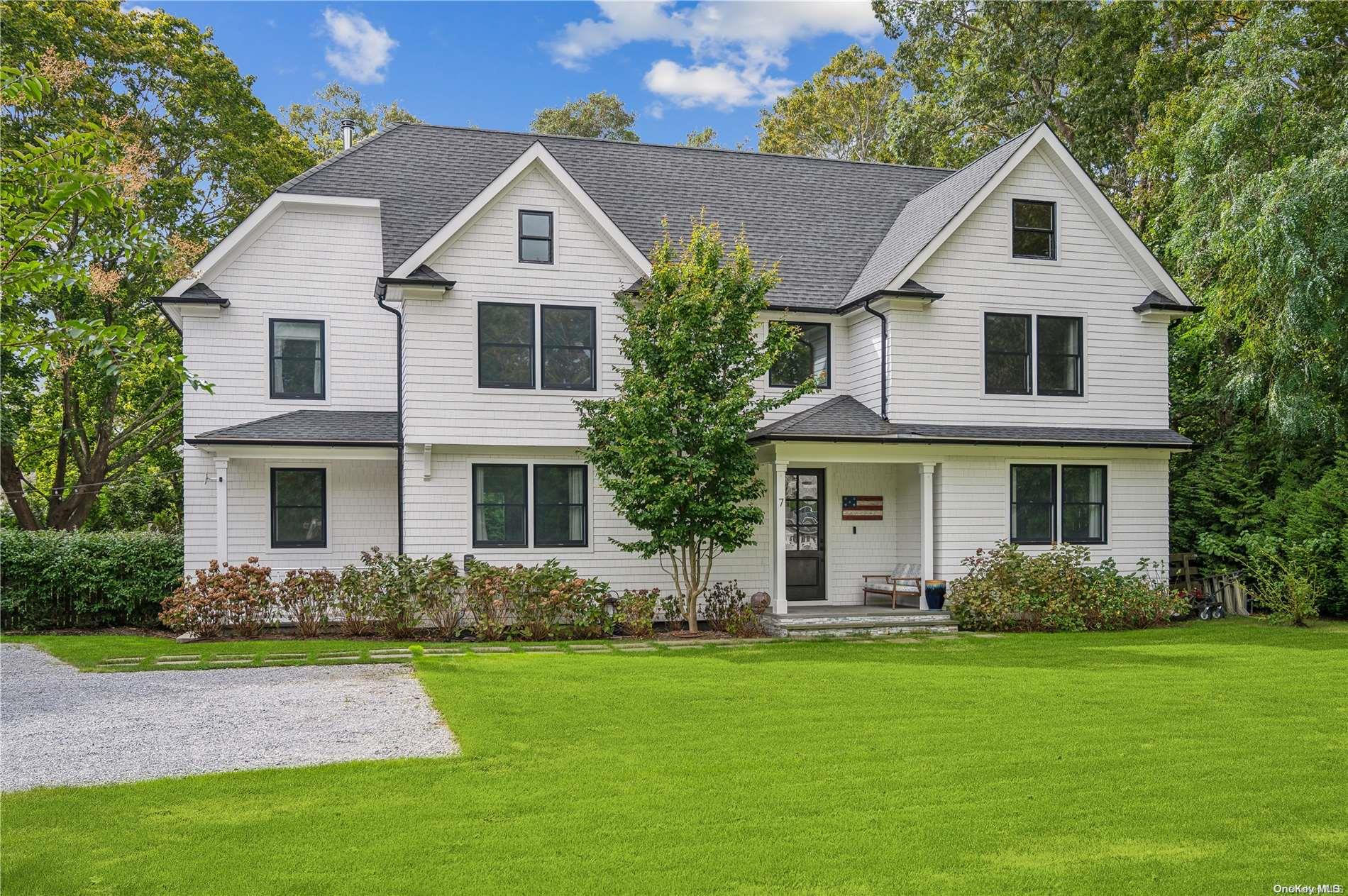 Two-story white shingle house with dark gables, covered entry, and broad green lawn.
