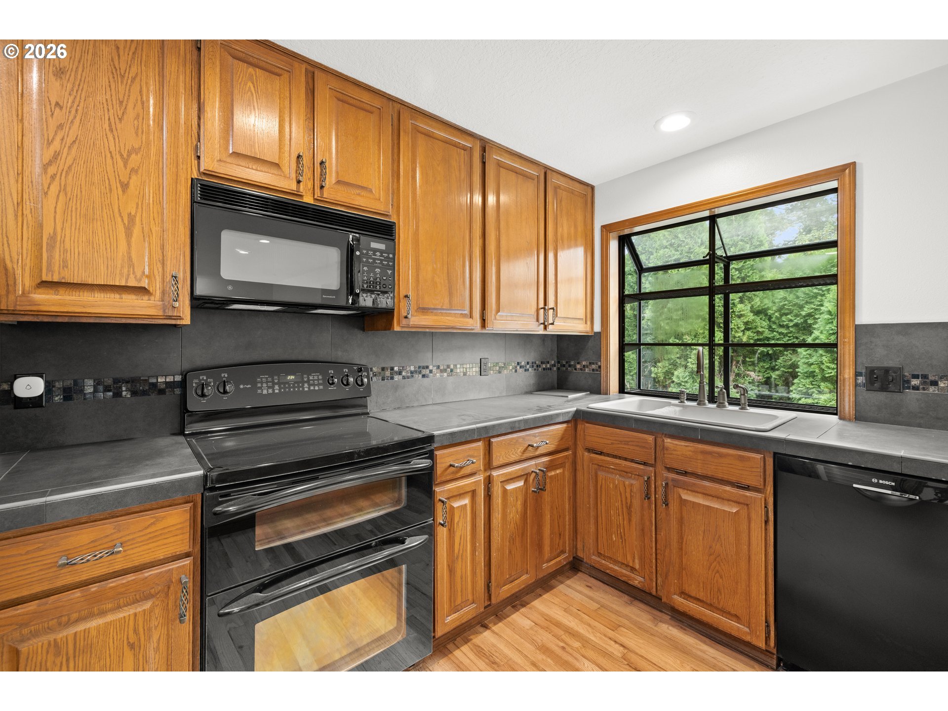 Kitchen with wooden cabinets, dark countertops, and a large window above the sink.