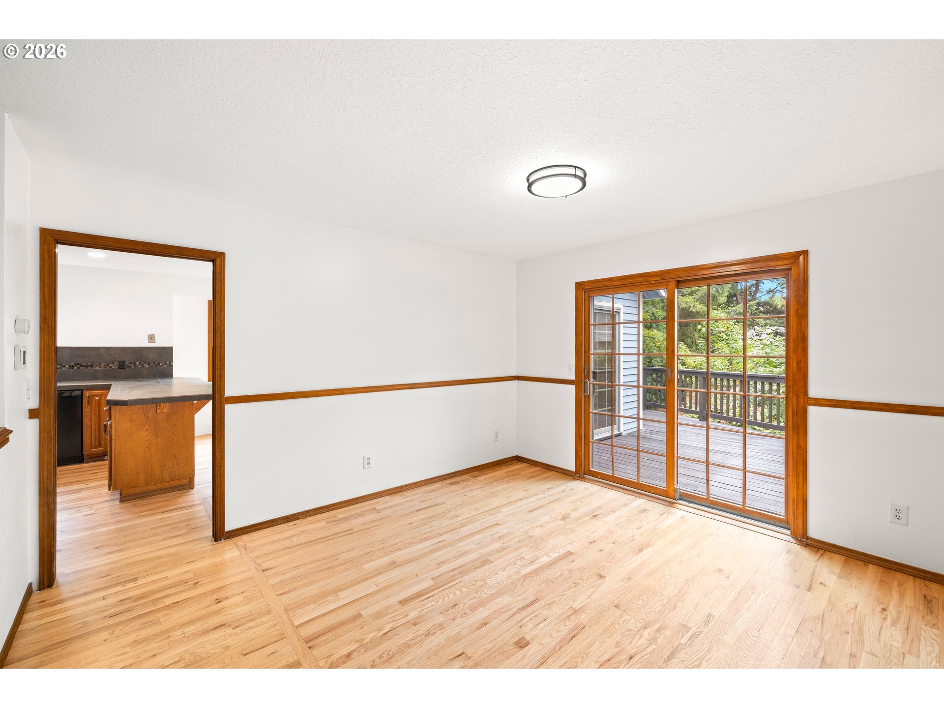 Empty dining room with hardwood floors, wood trim, and sliding glass doors opening onto a deck.