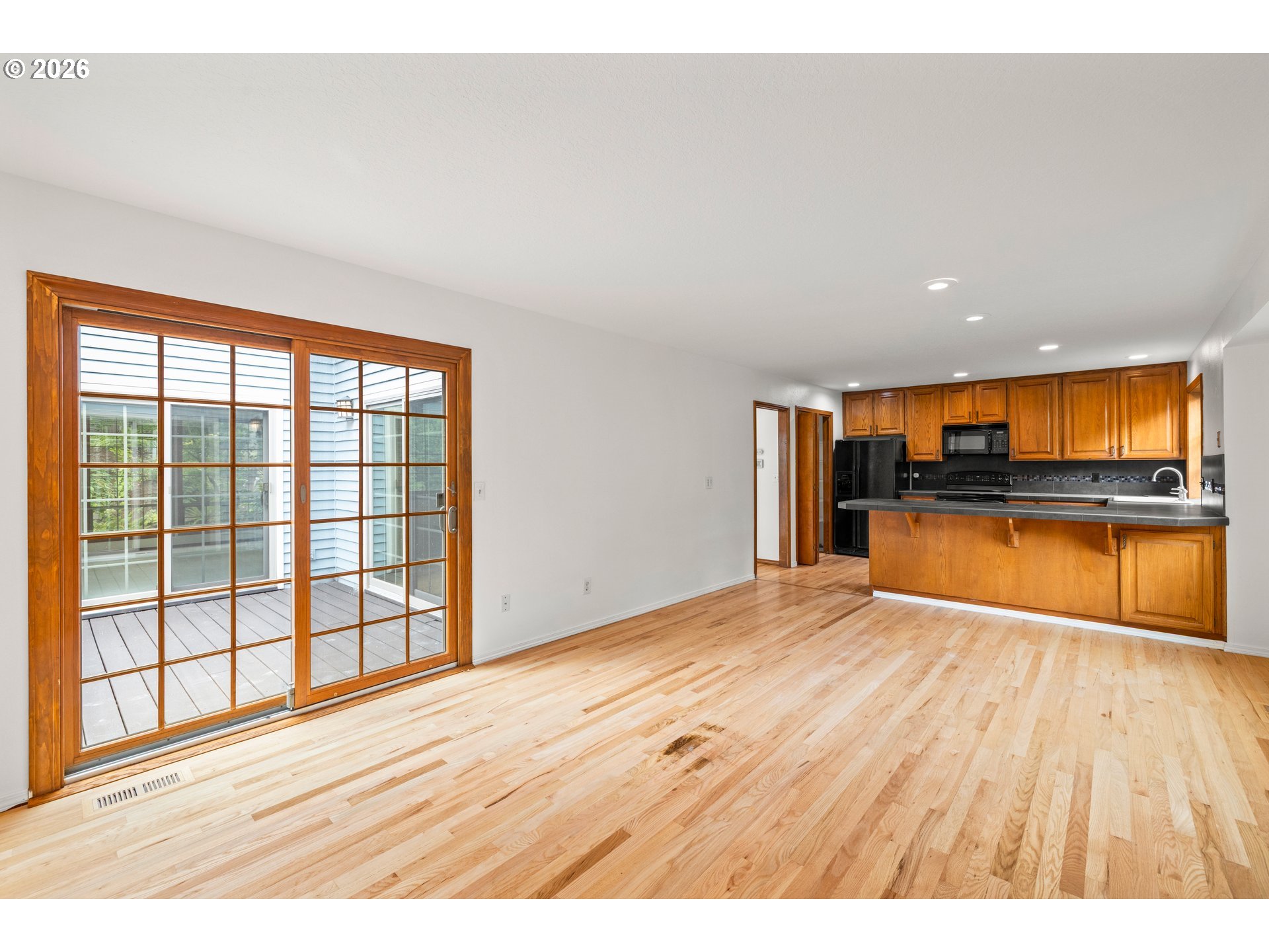 Open kitchen and dining area with warm wood cabinetry, hardwood floors, and sliding glass doors to a deck.