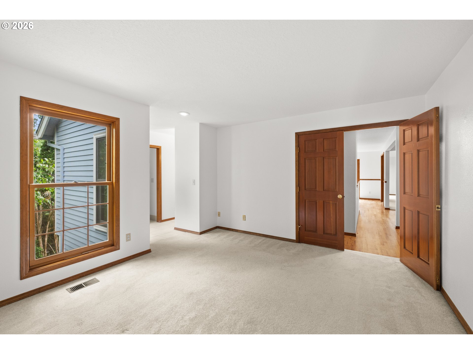 Empty carpeted bedroom with a large wood-trimmed window and open paneled doors.