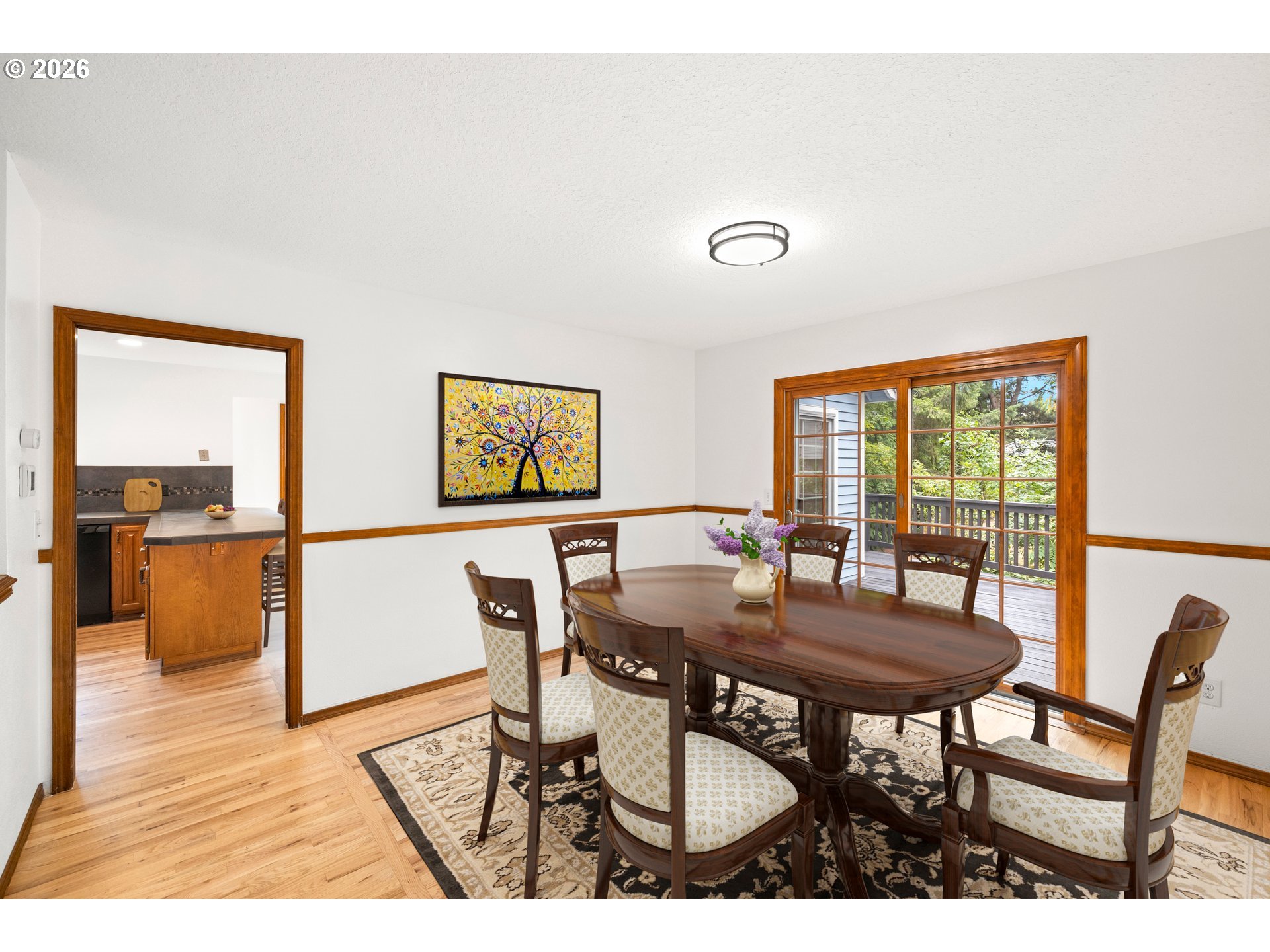 Dining room with a polished wood table, patterned rug, and glass doors opening to a deck.