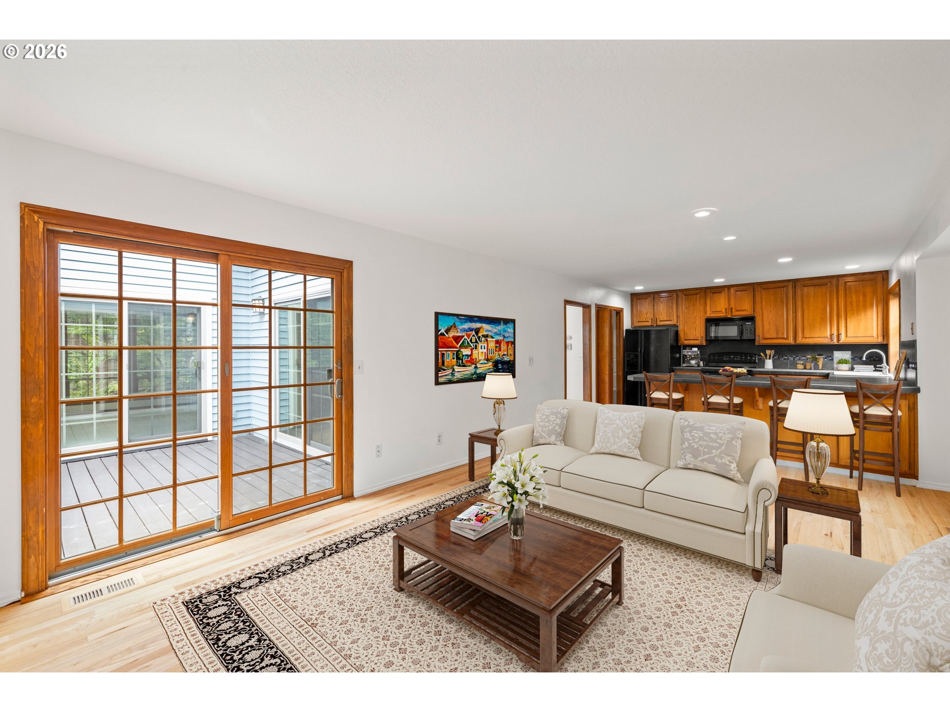Living room with wood-framed sliding doors to a deck and an open kitchen with warm wood cabinets.