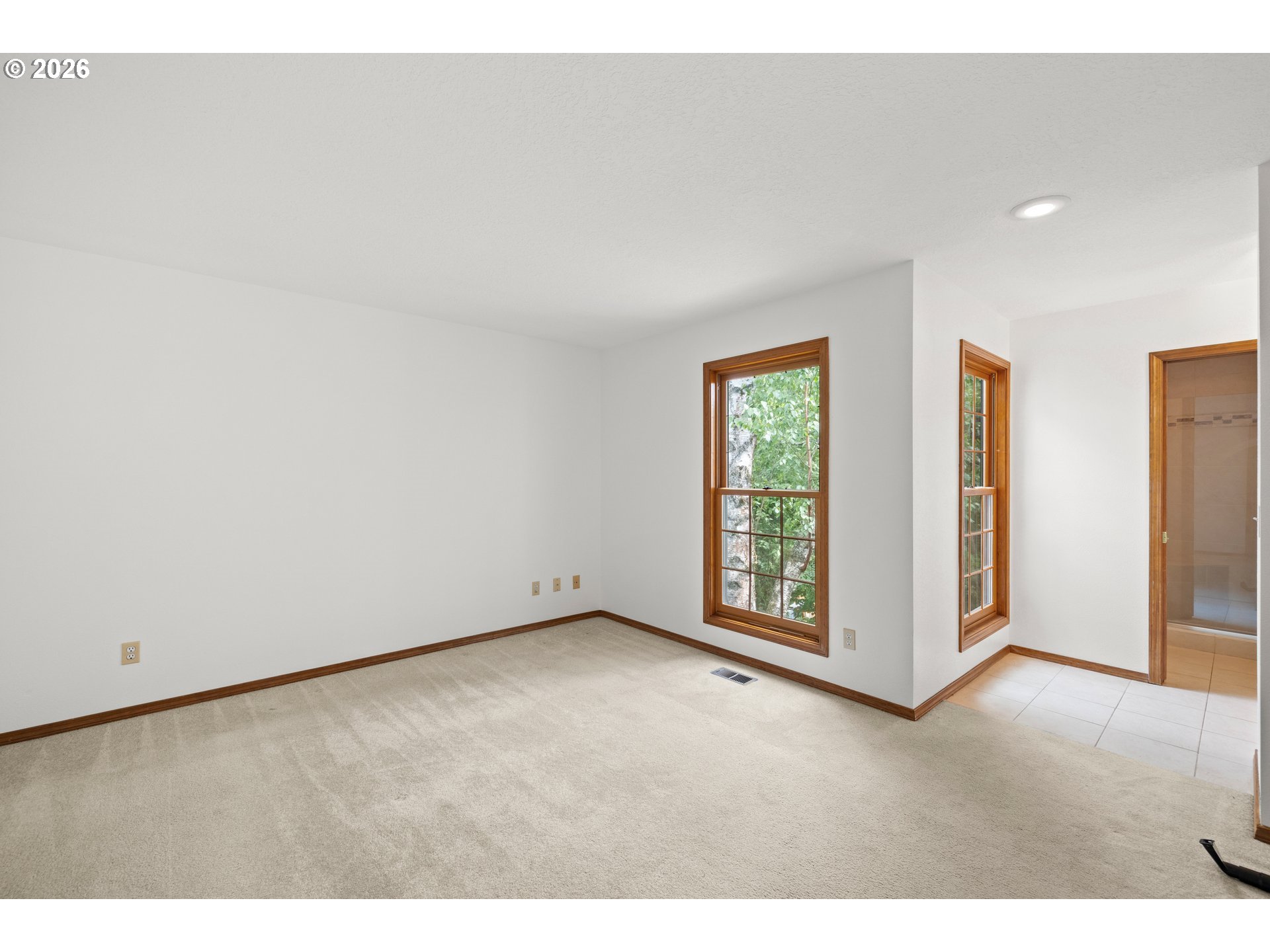 Vacant carpeted room with two tall wood-trimmed windows and an adjoining tiled area.