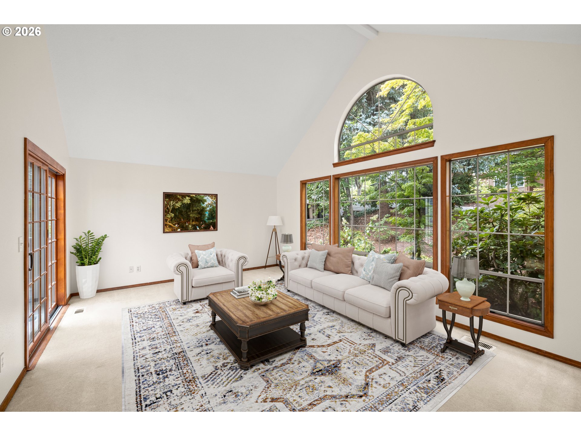 Living room with vaulted ceiling, white sofas, and tall windows overlooking greenery.
