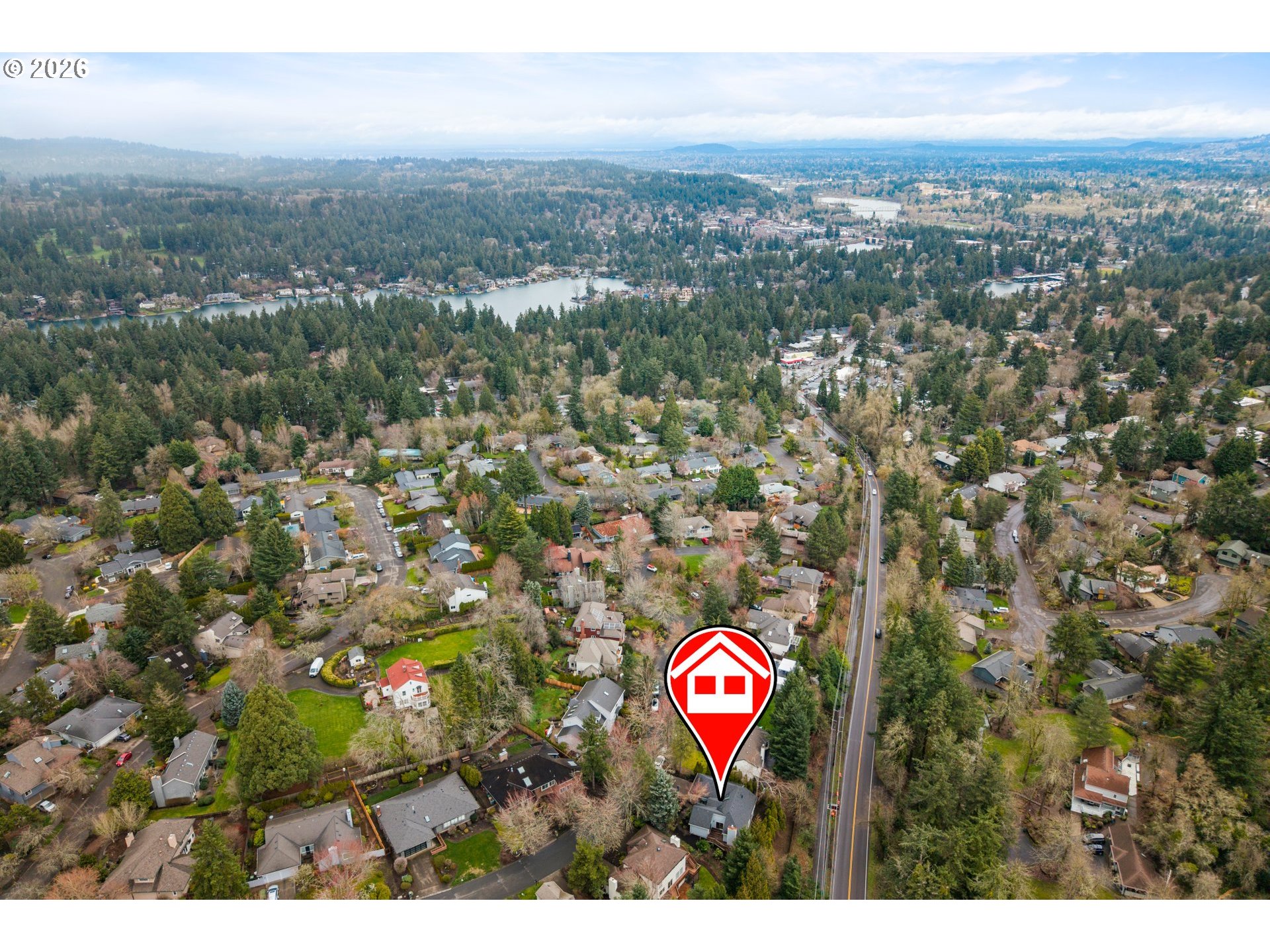 Aerial neighborhood view with a red house marker, wooded streets, and a lake in the distance.