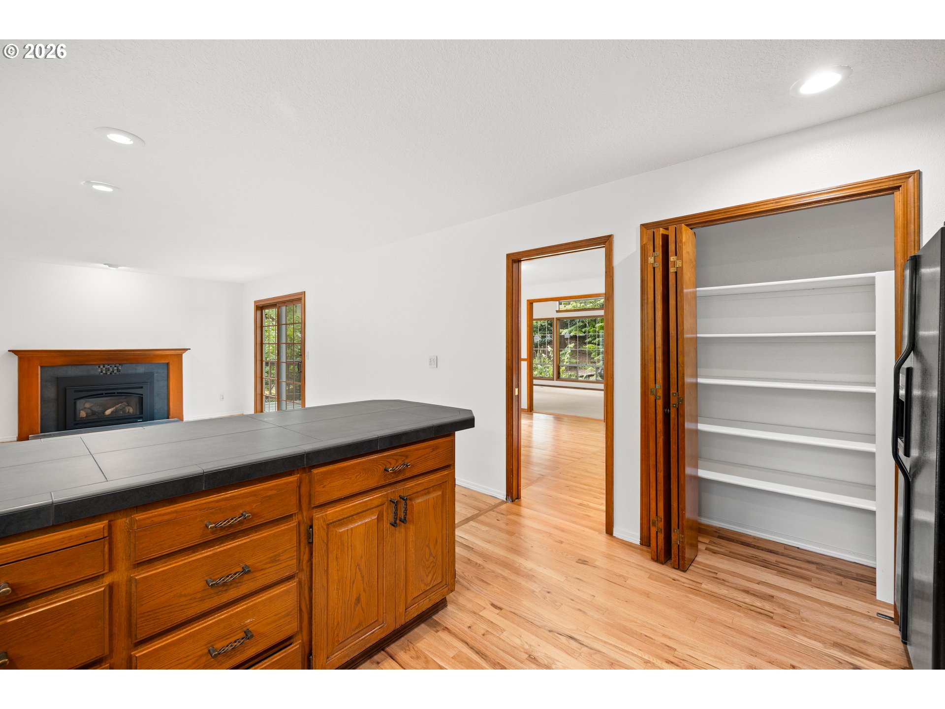 Kitchen with a tiled wood island, fireplace, hardwood floors, and open pantry shelves.