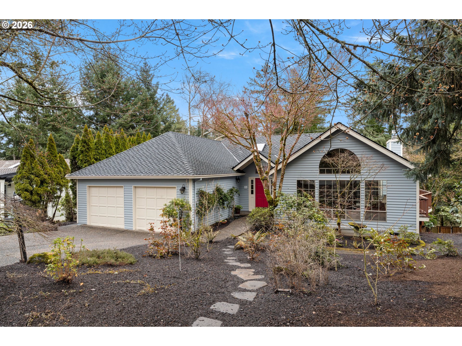 Gray-sided house with a red front door, double garage, and stepping-stone path through the front yard.