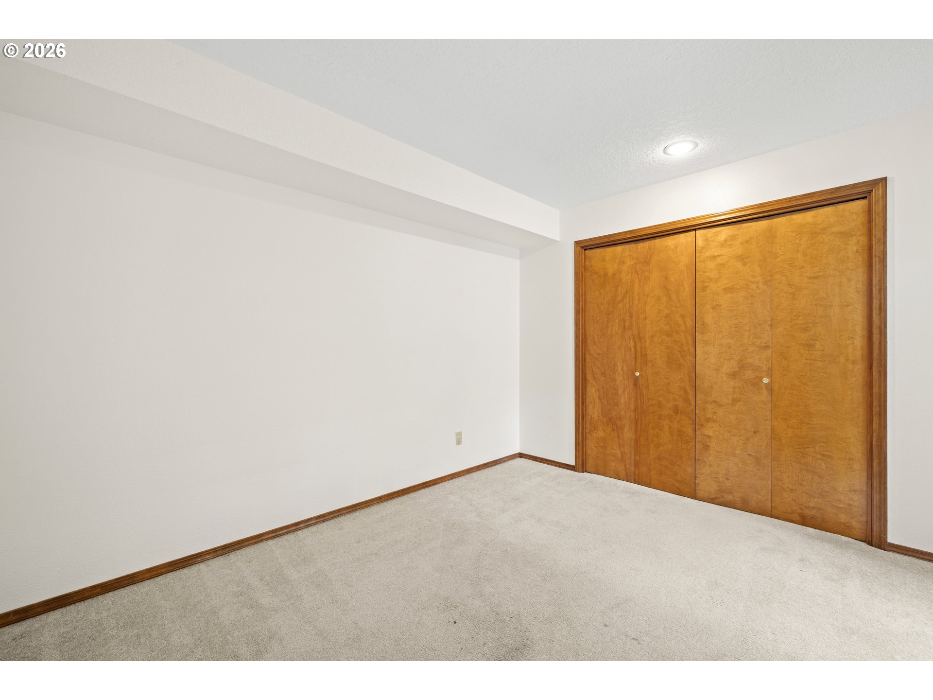 Empty bedroom with beige carpet and large wooden sliding closet doors.