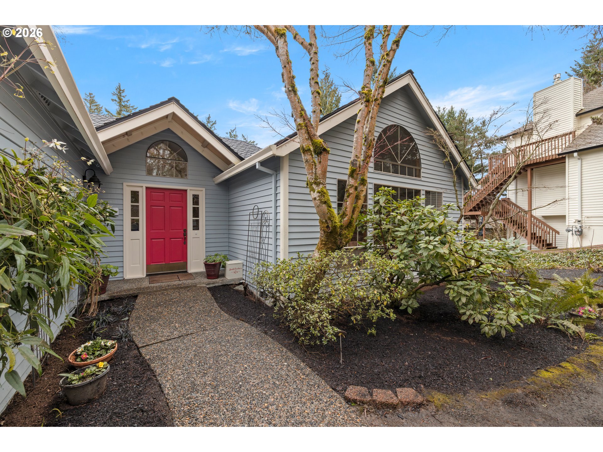 Gray-sided house with a red front door, arched windows, and a landscaped gravel walkway.