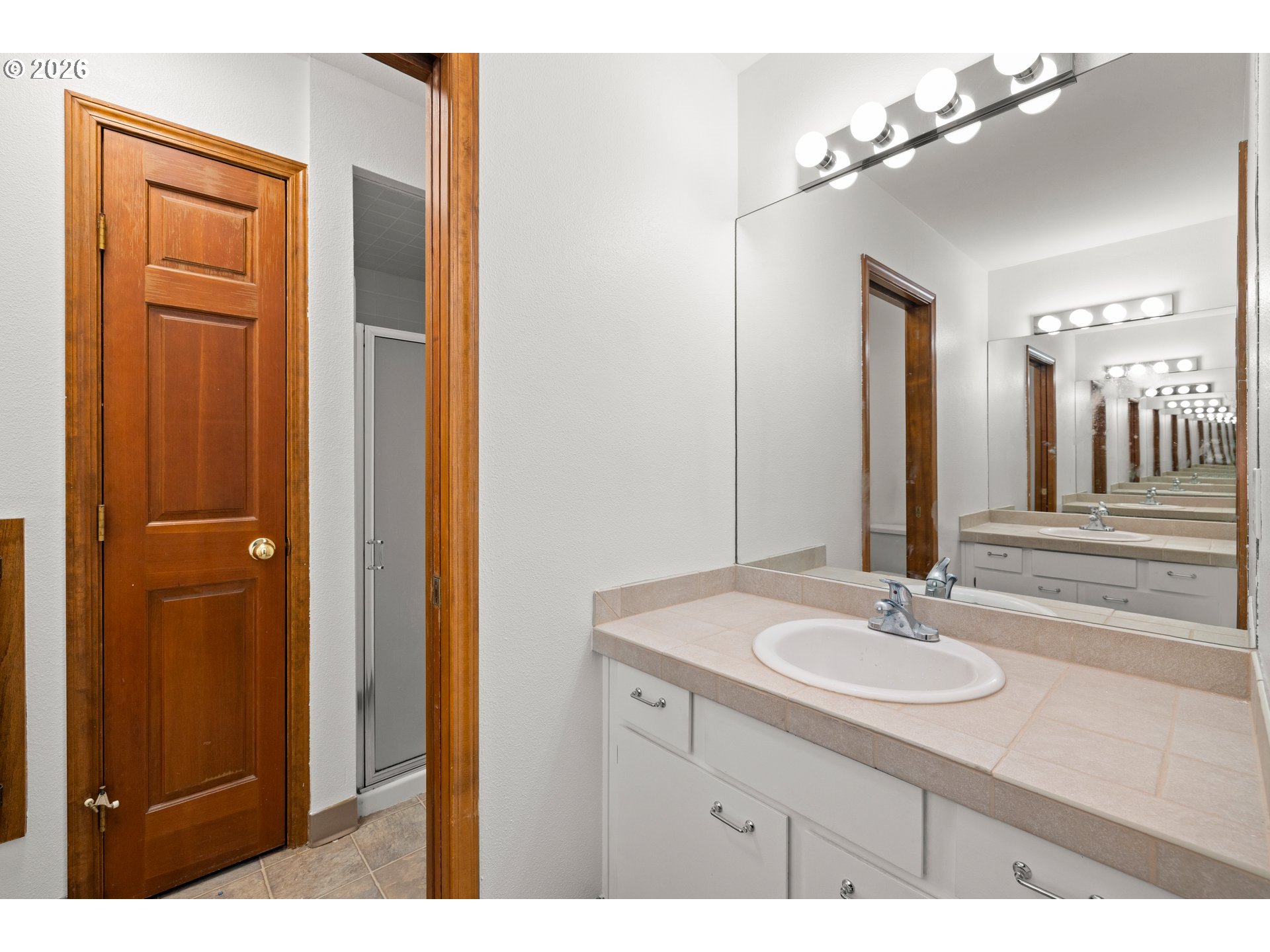 Bathroom vanity with tiled counter, oval sink, and large mirror reflecting vanity lights.