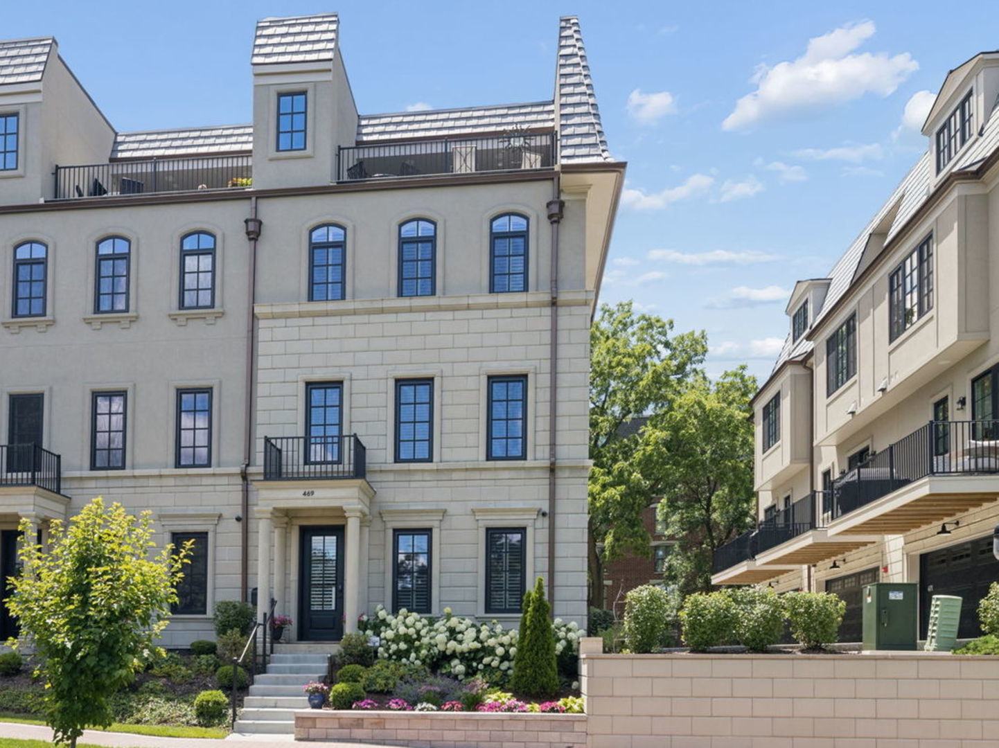 Pale stone townhouse with dark-framed windows, a small balcony, and landscaped entrance steps.