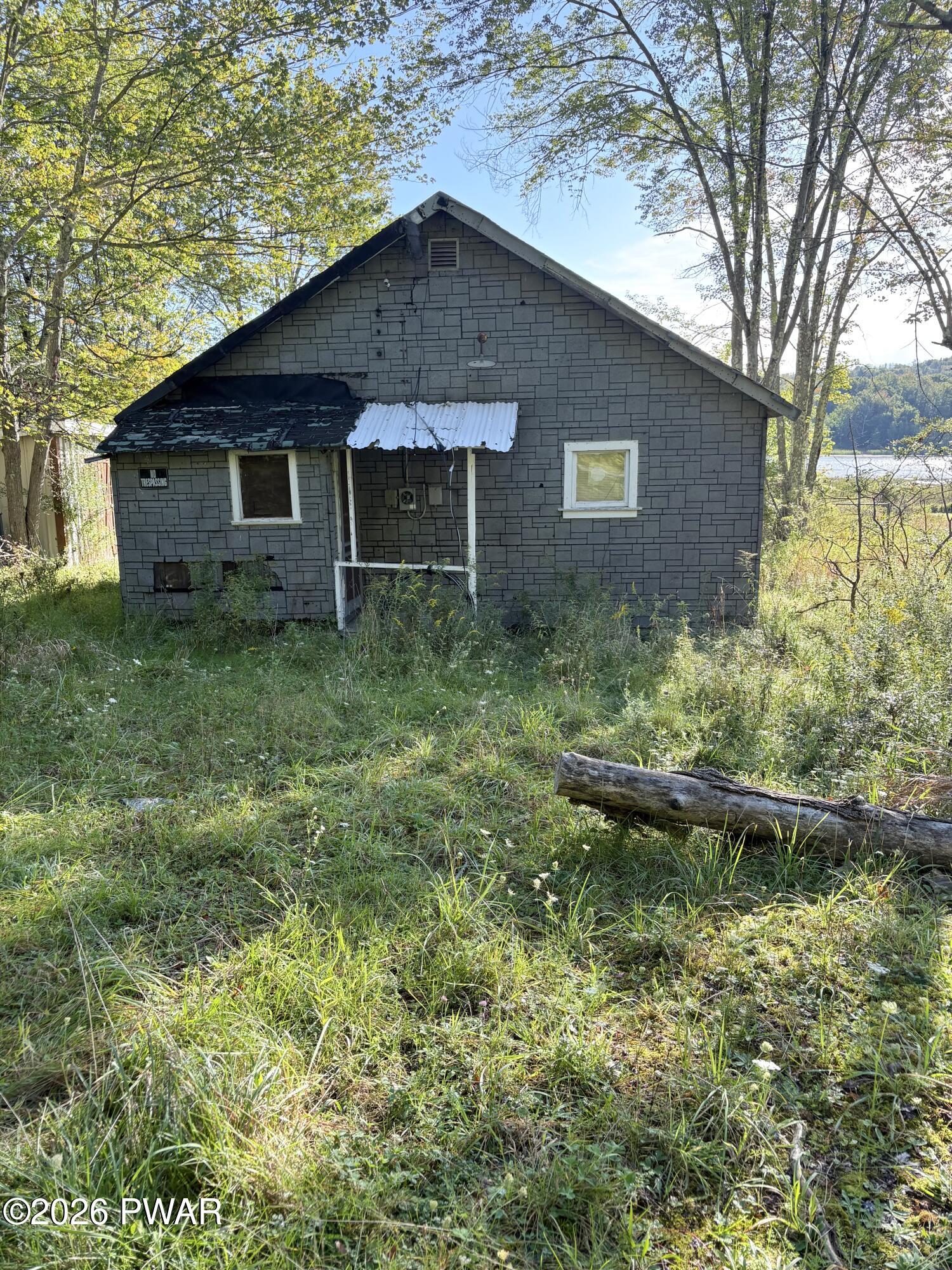 Gray-shingled house with a weathered awning in an overgrown yard, with a lake visible through the trees.
