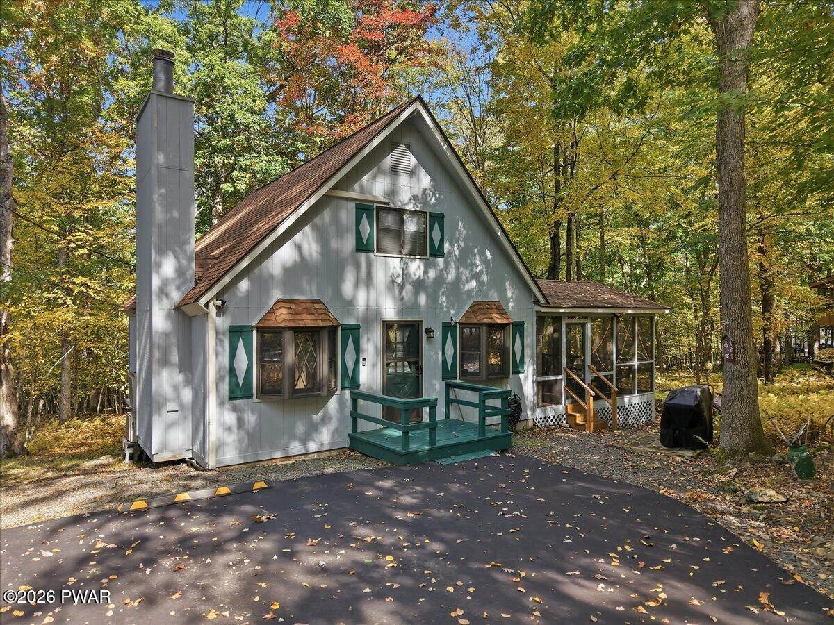 Gray cottage with green shutters and a small front deck among autumn trees.