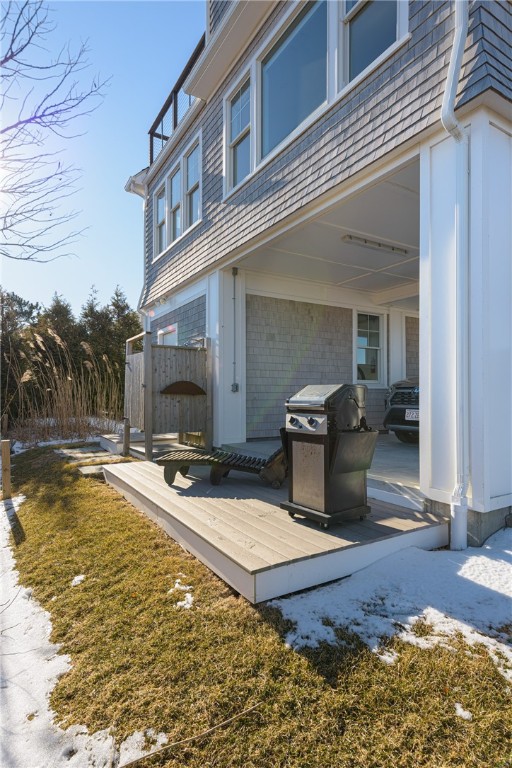Raised deck beneath the home’s upper level, with a barbecue grill and patches of snow in the yard.