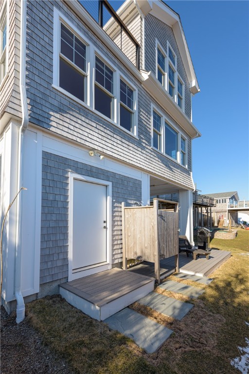Gray-shingled coastal home with white trim, ground-level decks, and a fenced patio.