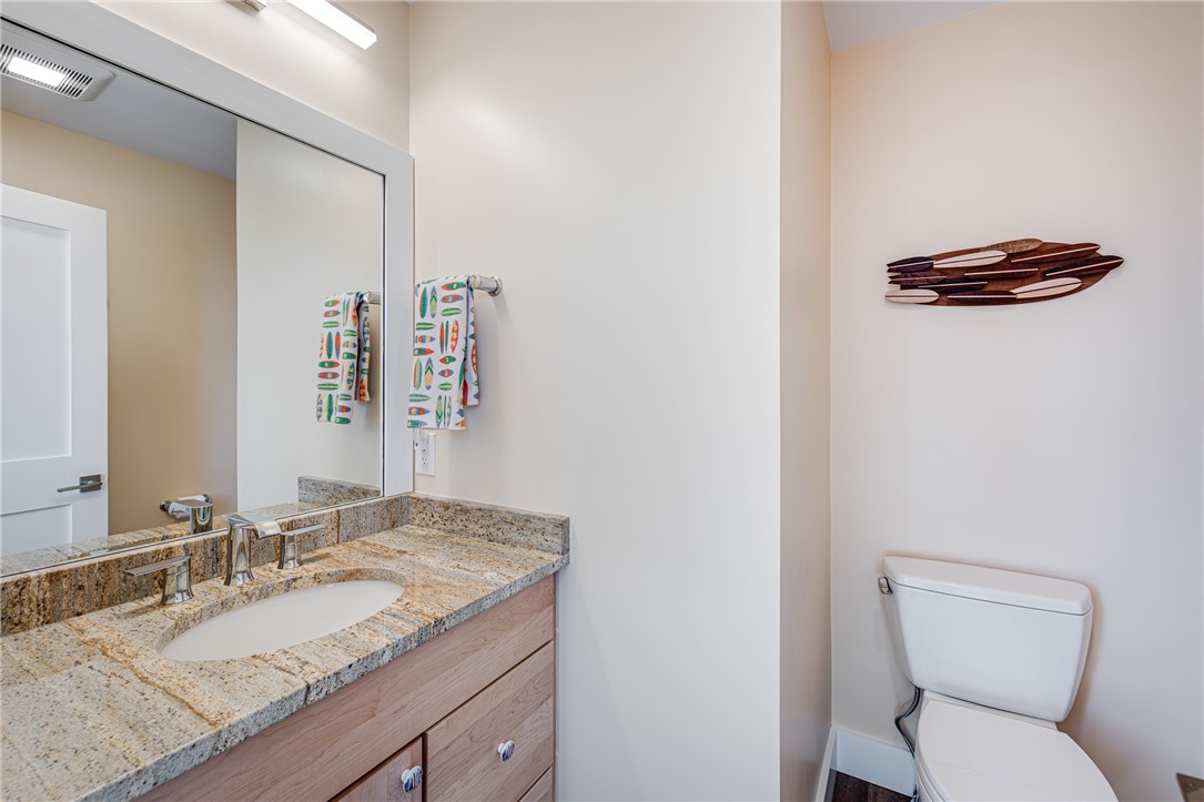 Bathroom with a granite vanity, large mirror, toilet, and surfboard-shaped wall decoration.