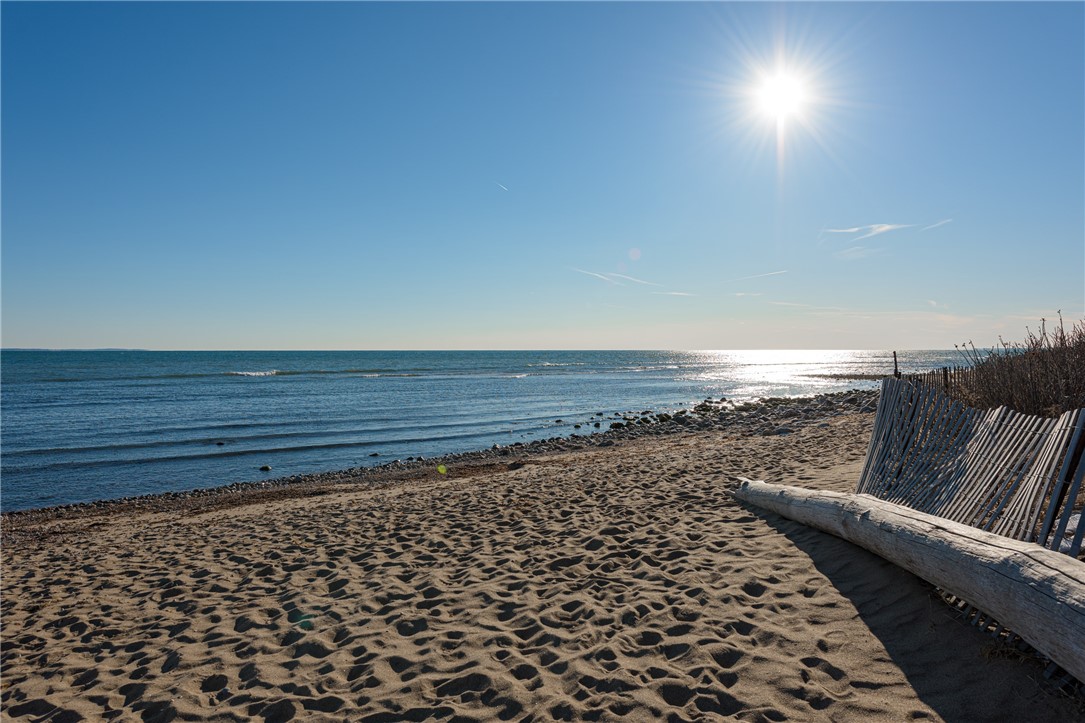 Sandy beach and calm ocean, with a driftwood log beside the beach fence.