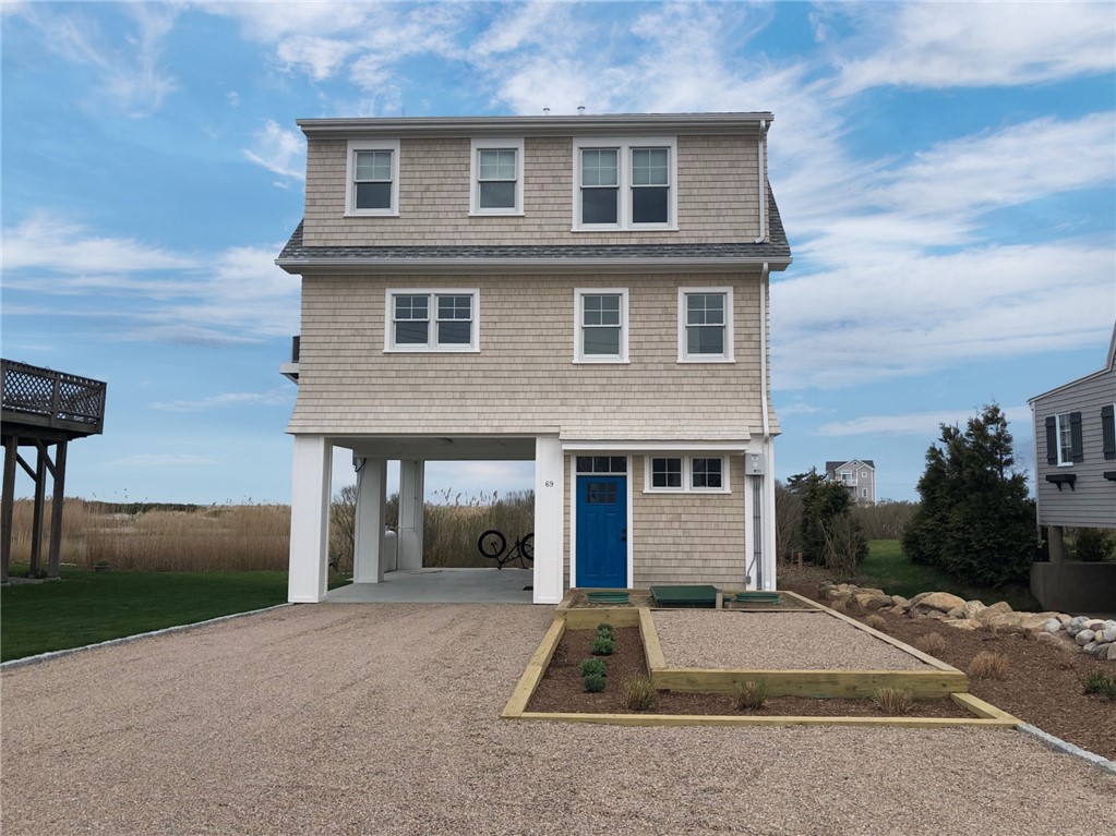 Three-story shingle-sided coastal home with a blue front door and gravel driveway.