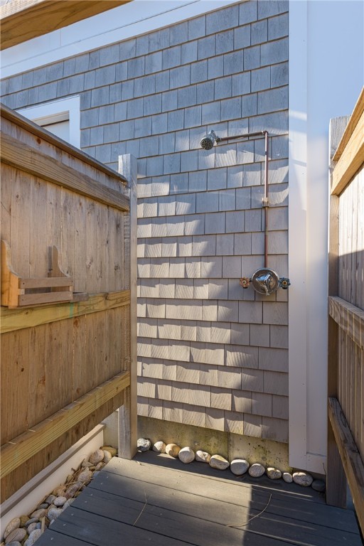Outdoor shower against cedar shingles, enclosed by wooden privacy fencing with smooth stones at the base.