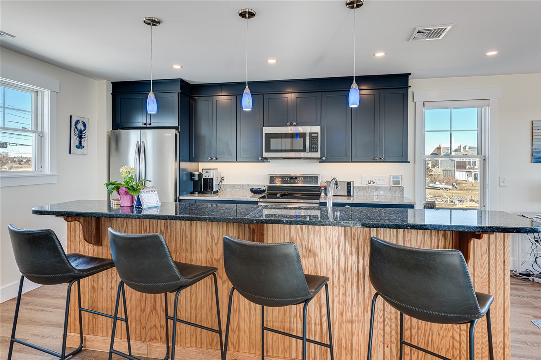 Modern kitchen with navy cabinets, stainless appliances, and a wood-paneled island with four bar stools.