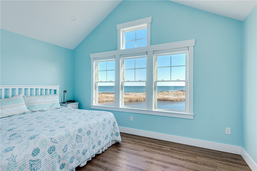 Bedroom with turquoise walls and a white bed overlooking the ocean through large windows.