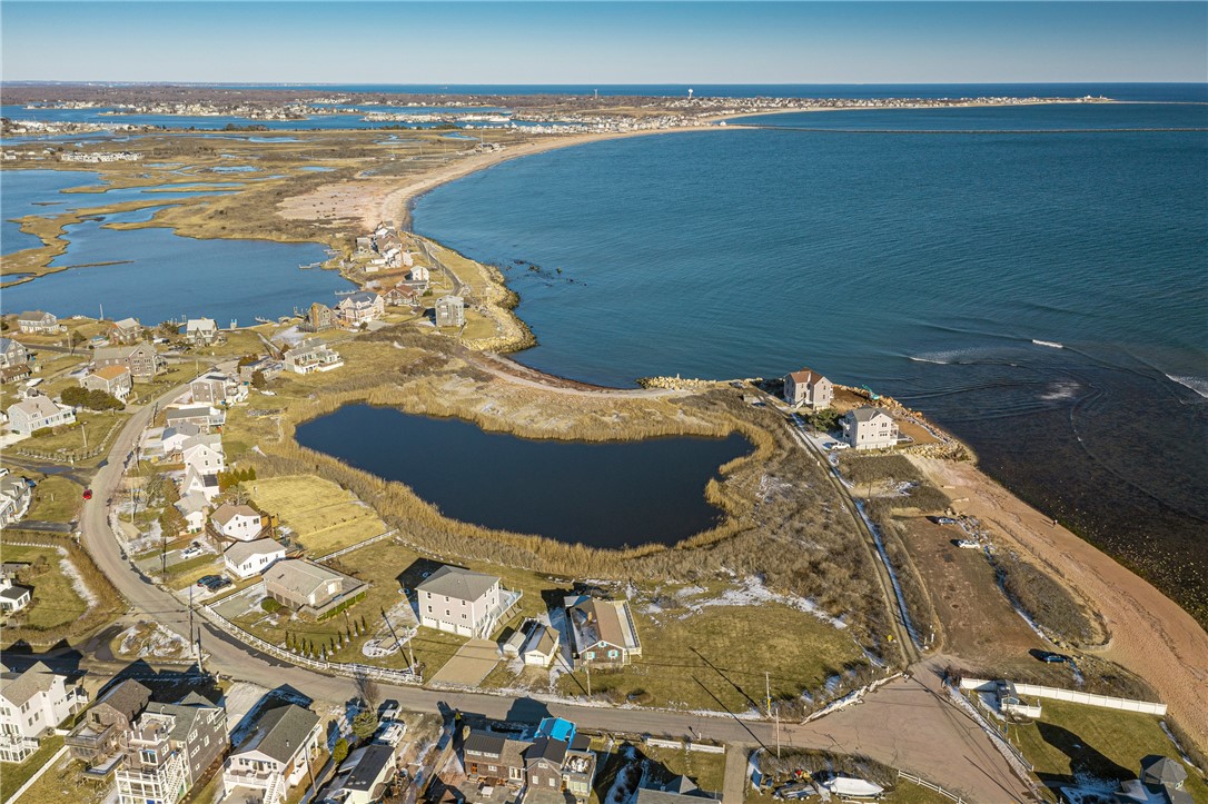 Aerial coastal neighborhood with oceanfront homes, a curved shoreline, and a salt marsh pond.