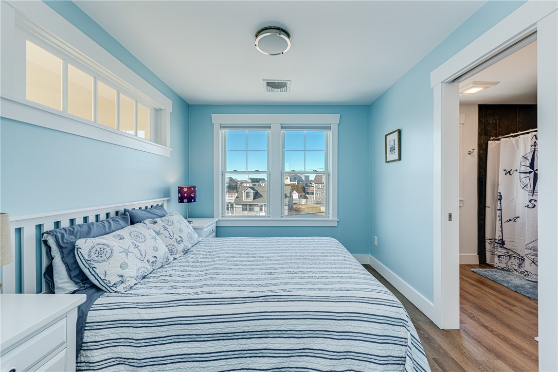 Bedroom with blue walls, nautical bedding, and windows overlooking neighboring homes.