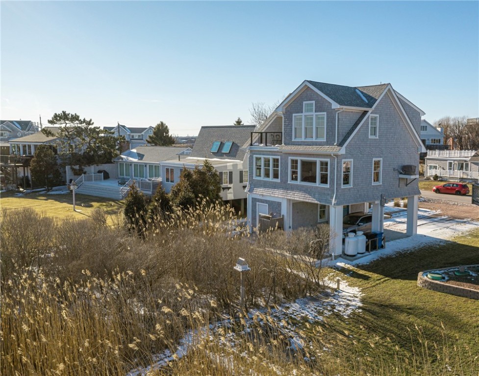 Gray-shingled coastal home raised above ground, with marsh grasses and patches of snow in the foreground.