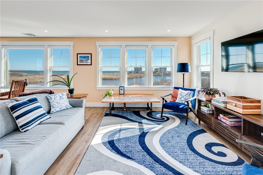 Furnished living room with broad windows overlooking the water and a blue-and-white patterned rug.
