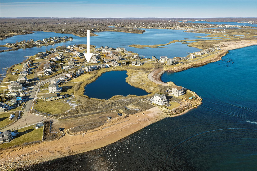 Aerial view of the coastal home marked by an arrow, beside a pond and sandy shoreline.