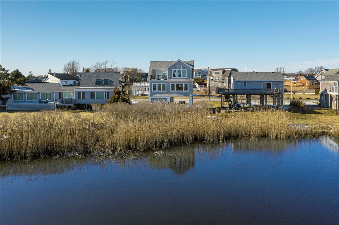 Coastal home with a balcony and large windows, viewed across marsh grass and water.