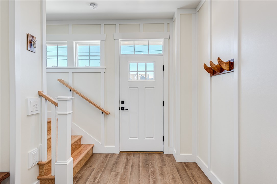 Entry foyer with a windowed white front door, hardwood stairs, and natural wood railings.