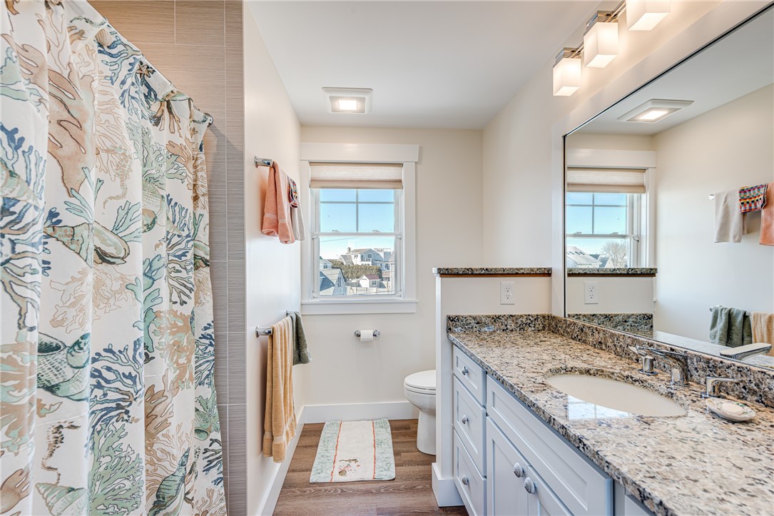 Bathroom with granite vanity, patterned shower curtain, and a window overlooking rooftops.