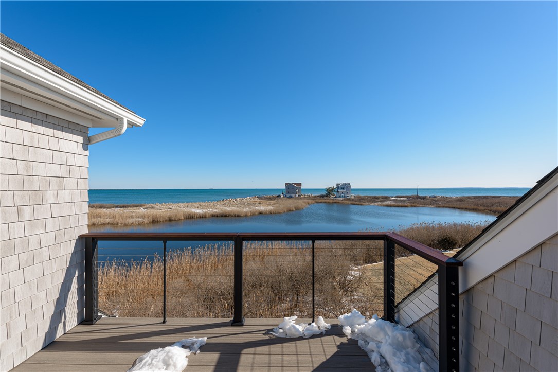 Raised deck overlooking a tidal pond, salt marsh, and ocean, with patches of snow on the boards.